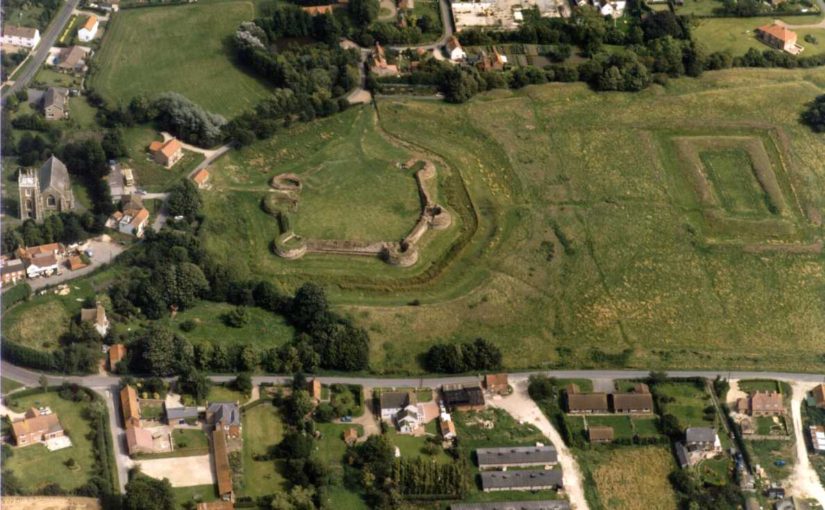 Aerial photo of a green field surrounded by houses. At one end of the field stand the remains of a hexagonal castle.
